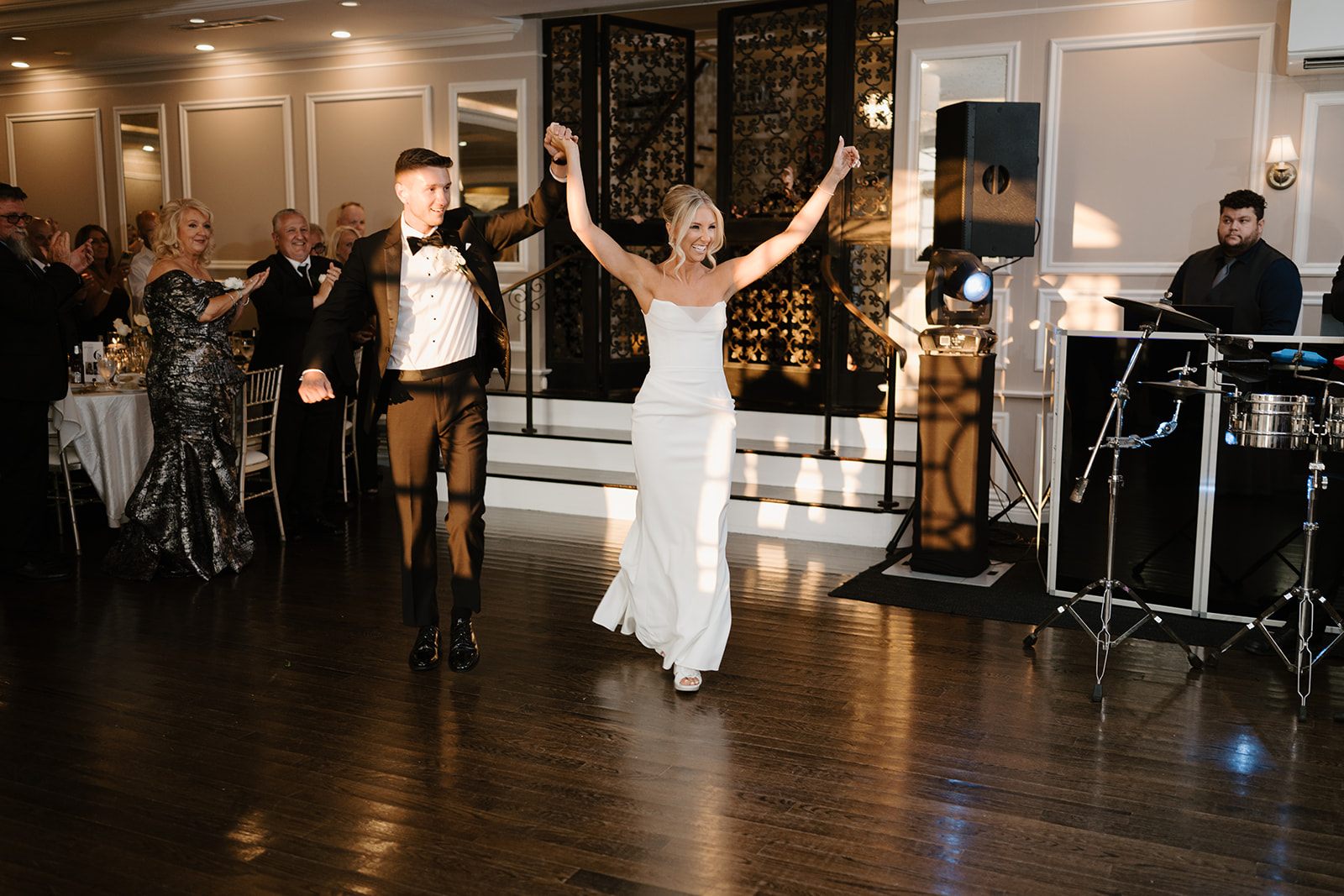 Bride and groom make a joyful grand entrance into their reception, holding hands high as guests cheer.